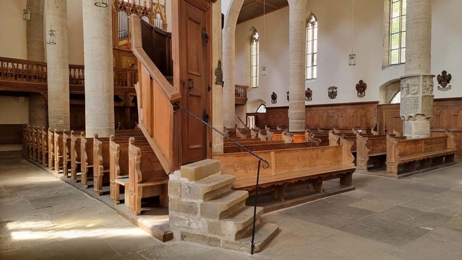 View into the church with wooden pews, wooden pulpit, stone columns,
